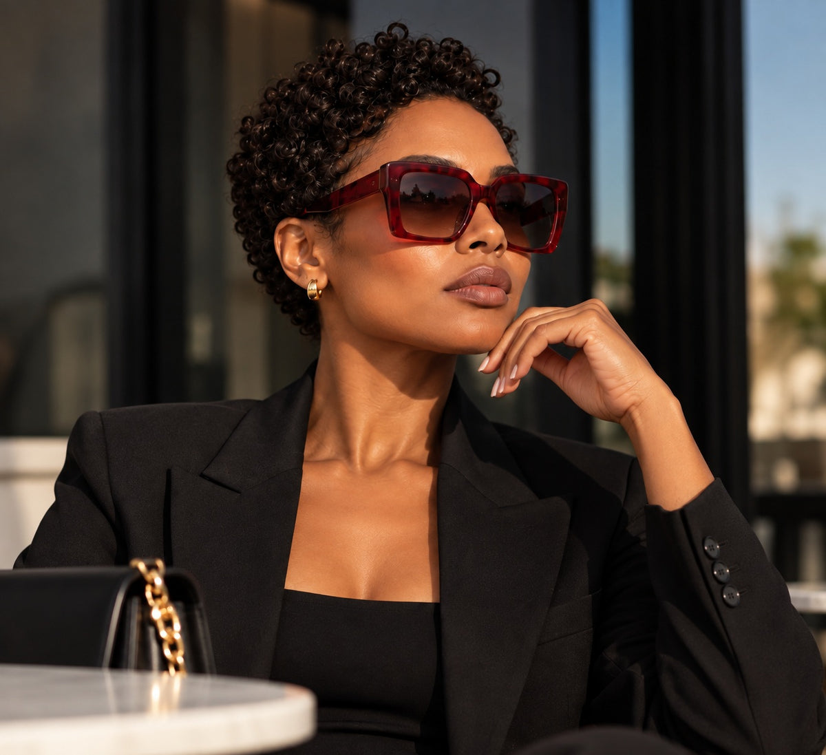 Woman in a black blazer wearing cherry square sunglasses at a café.